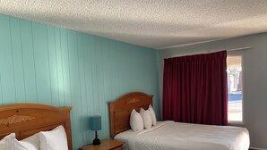 Une chambre d’hôtel avec deux lits, une tête de lit en bois, une table de chevet avec une lampe et une fenêtre avec des rideaux rouges.