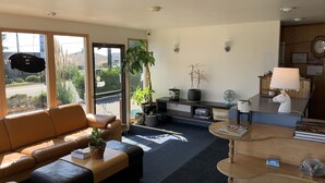 Un salon moderne avec un canapé en cuir, une table basse et une table à manger agrémentée d’une lampe. On y trouve également des plantes en pot et, grâce aux grandes fenêtres, une vue sur la rue.