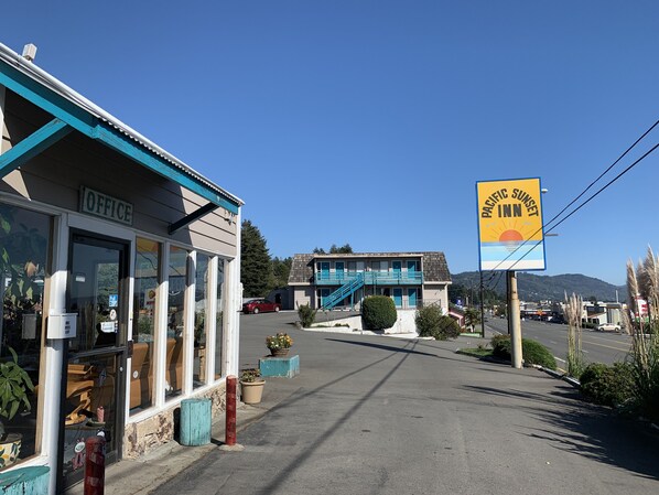 A building with a sign for Pacific Sunset Inn, a small office, and a red car parked outside.