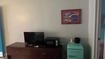 A hotel room with a bed, a desk with a computer, a microwave, and a teal-colored refrigerator.