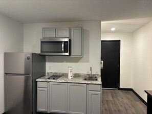 A compact kitchen with a stainless steel refrigerator, a microwave, and a granite countertop. - StayInn - Grand Forks (Grand Forks)