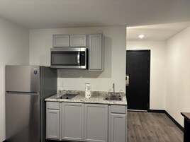 Cocina compacta con refrigerador de acero inoxidable, microondas y encimera de granito.