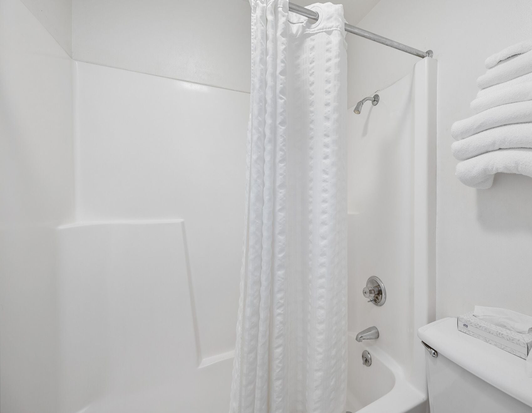 A white bathroom with a shower curtain, a toilet, and a stack of white towels.