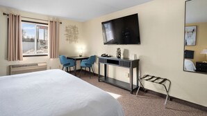 Een hotelkamer met een bed, een bureau, twee stoelen, een televisie en een raam met gordijnen.