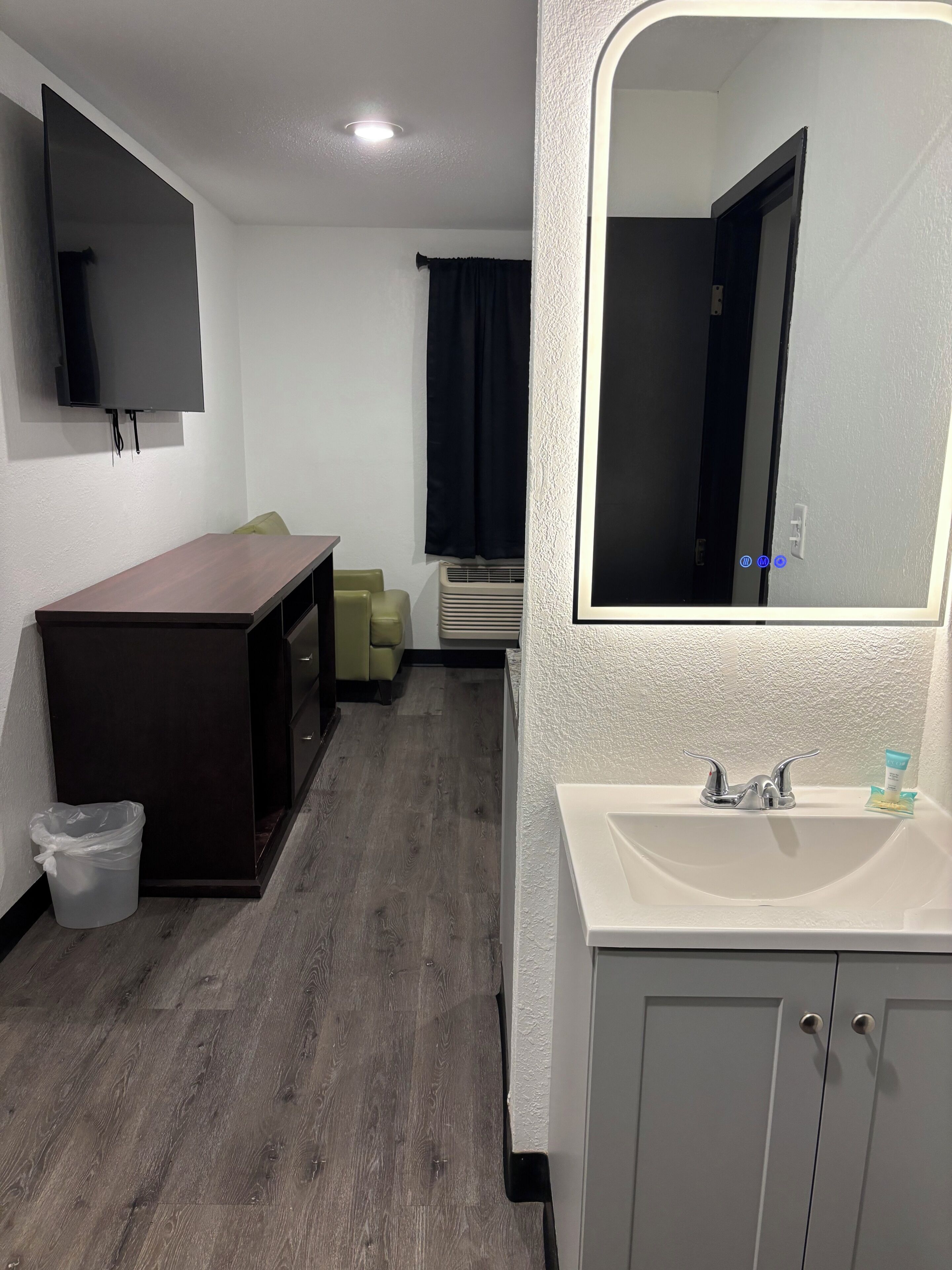 Une chambre d’hôtel avec un bureau en bois, une télévision, un miroir, un lavabo et un placard.