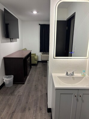 A hotel room with a wooden desk, a television, a mirror, a sink, and a cabinet. - StayInn - Grand Forks (Grand Forks)