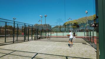 Una cancha de tenis con red, rodeada por una valla, y equipada con iluminación artificial.