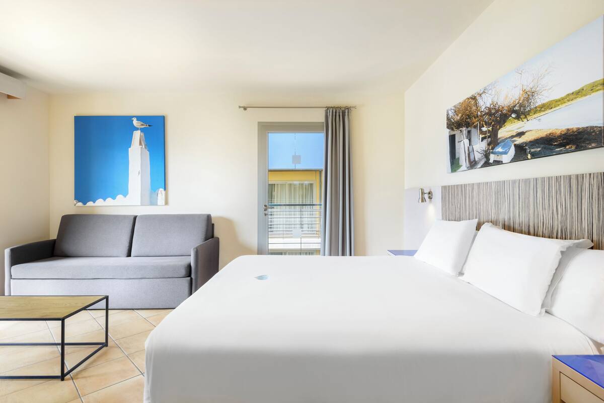 Une chambre d’hôtel avec un lit, un canapé, une table basse et des œuvres d’art accrochées aux murs.