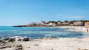 A coastal town with buildings along the shore, clear blue water, and a sandy beach.