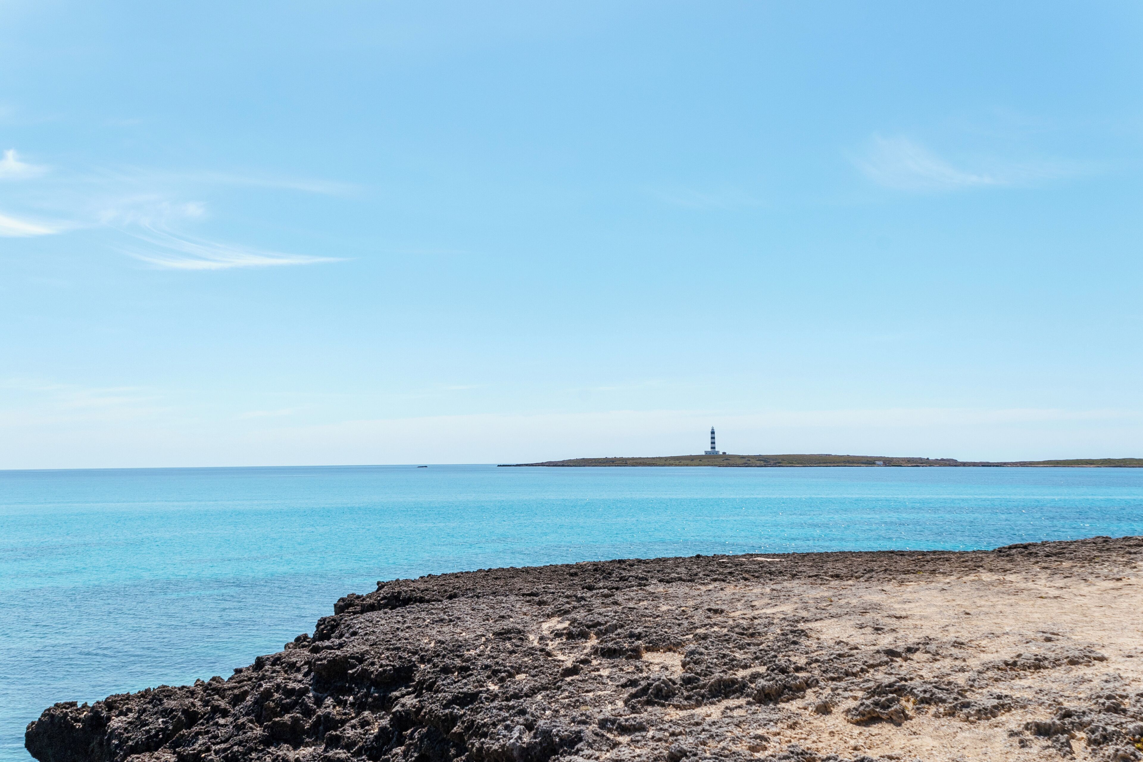 A coastal landscape with a rocky shoreline, a lighthouse in the distance, and calm blue waters.