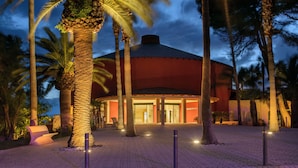 A building with a dome structure, surrounded by palm trees, and a paved walkway.