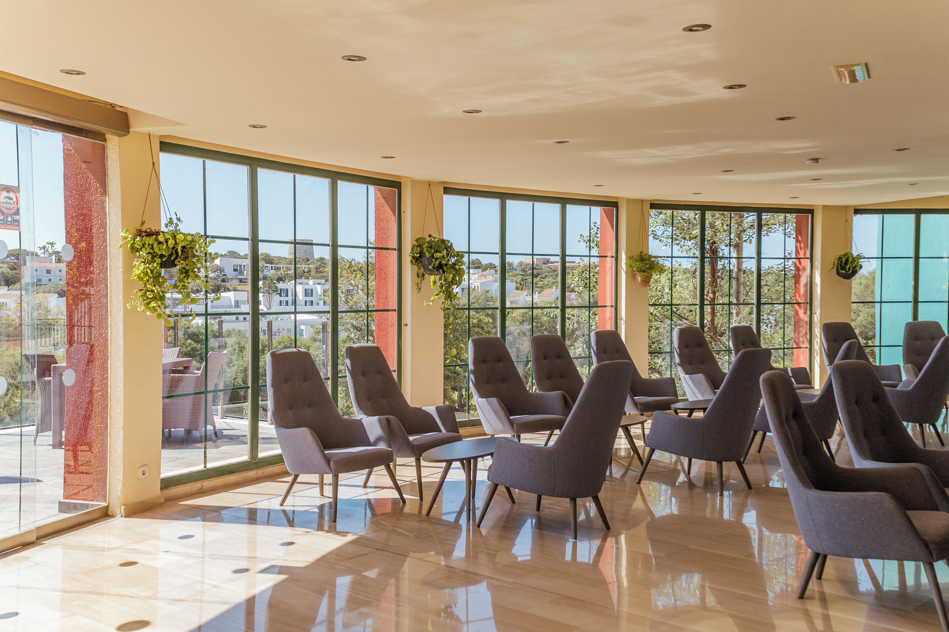 A spacious indoor area with large windows, modern chairs, and hanging plants.