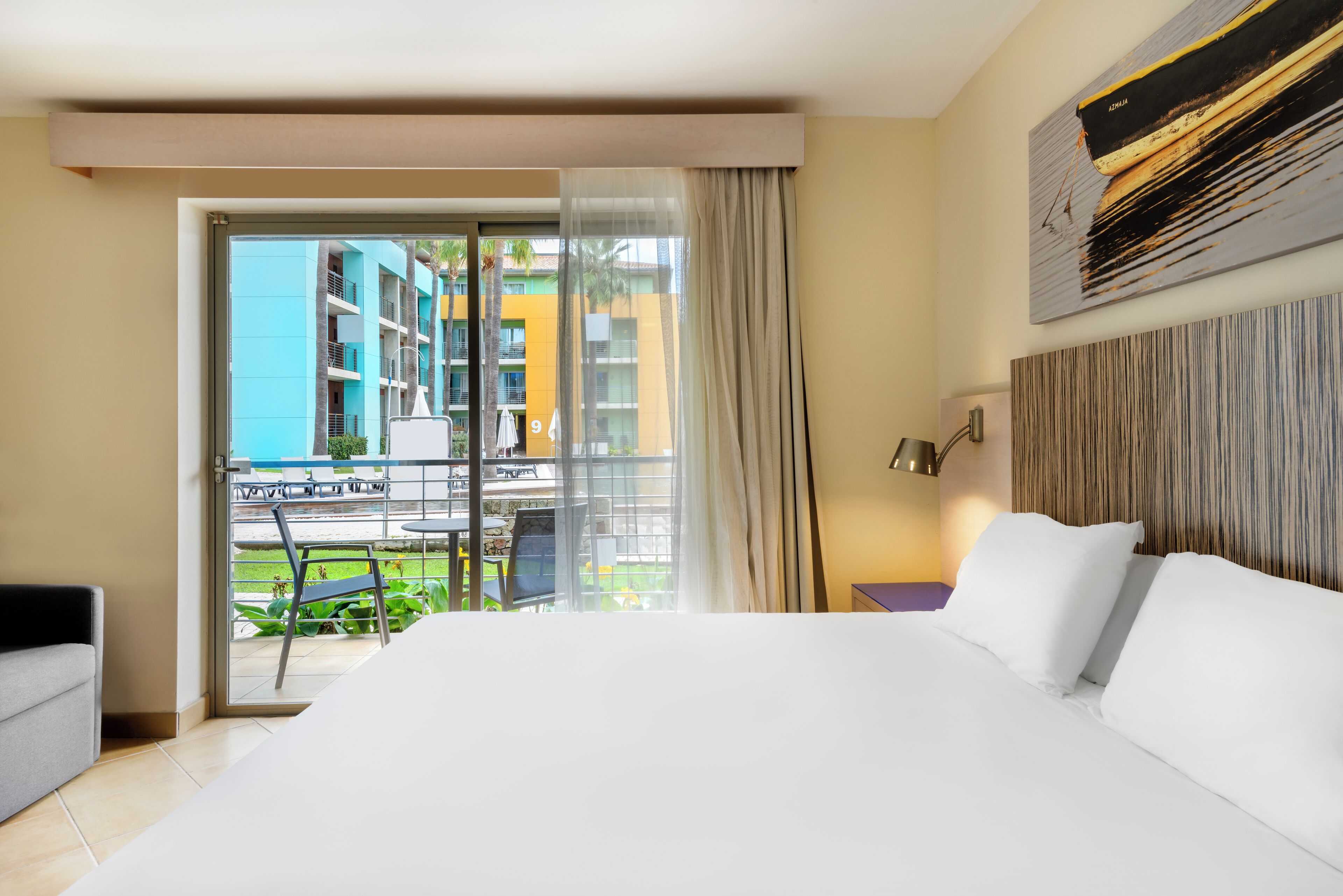 A hotel room with a large bed, a view of a balcony, and a dining area outside.