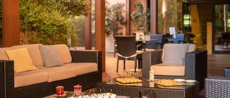 An outdoor seating area with wicker furniture, a glass-top table with appetizers, and a view of the garden.