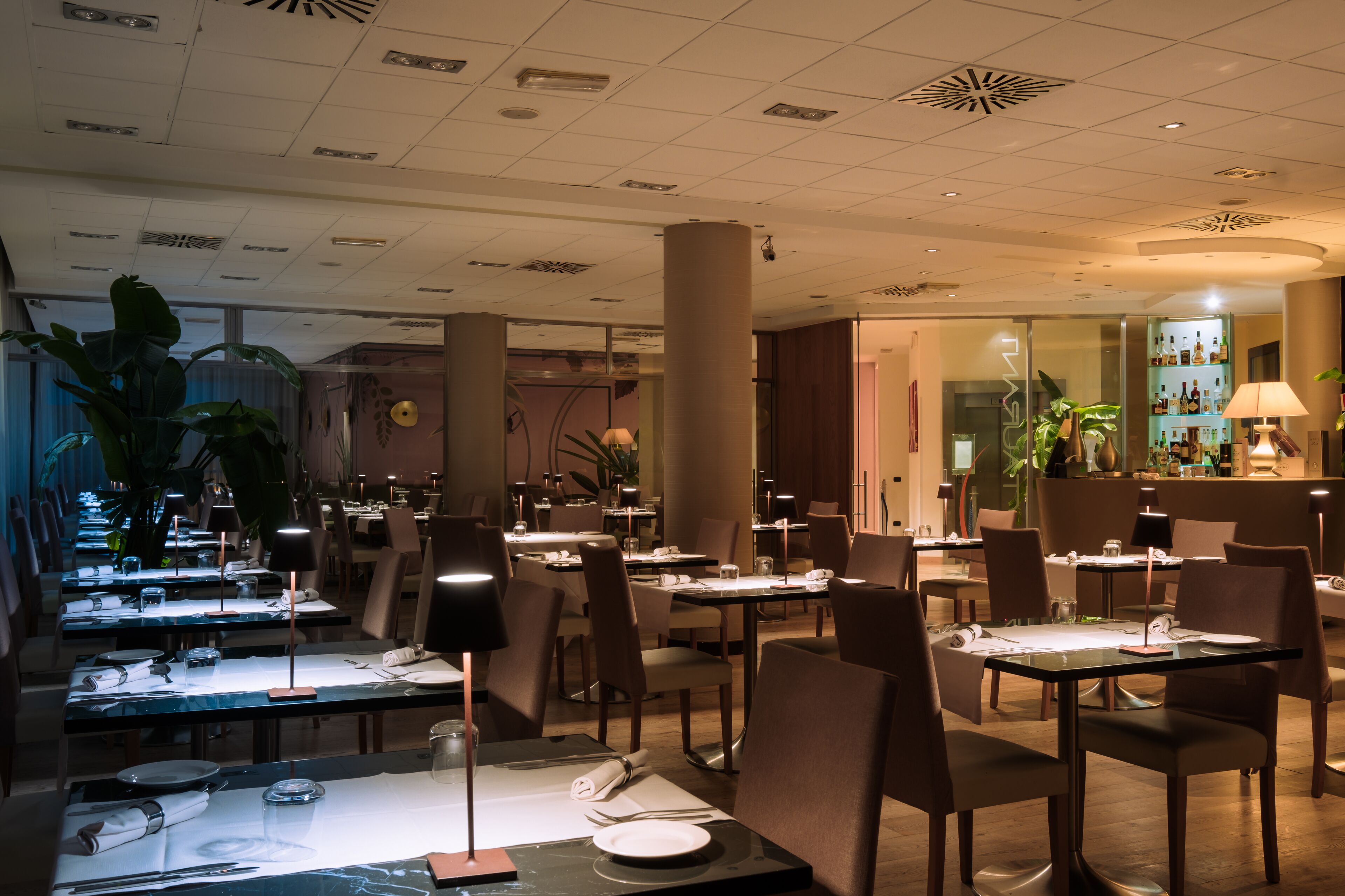 Un ristorante con tavoli apparecchiati, sedie e un'area bar con scaffali pieni di bottiglie.