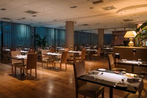 Een ruim restaurant met meerdere tafels en stoelen, een houten vloer en een grote plant in het midden.