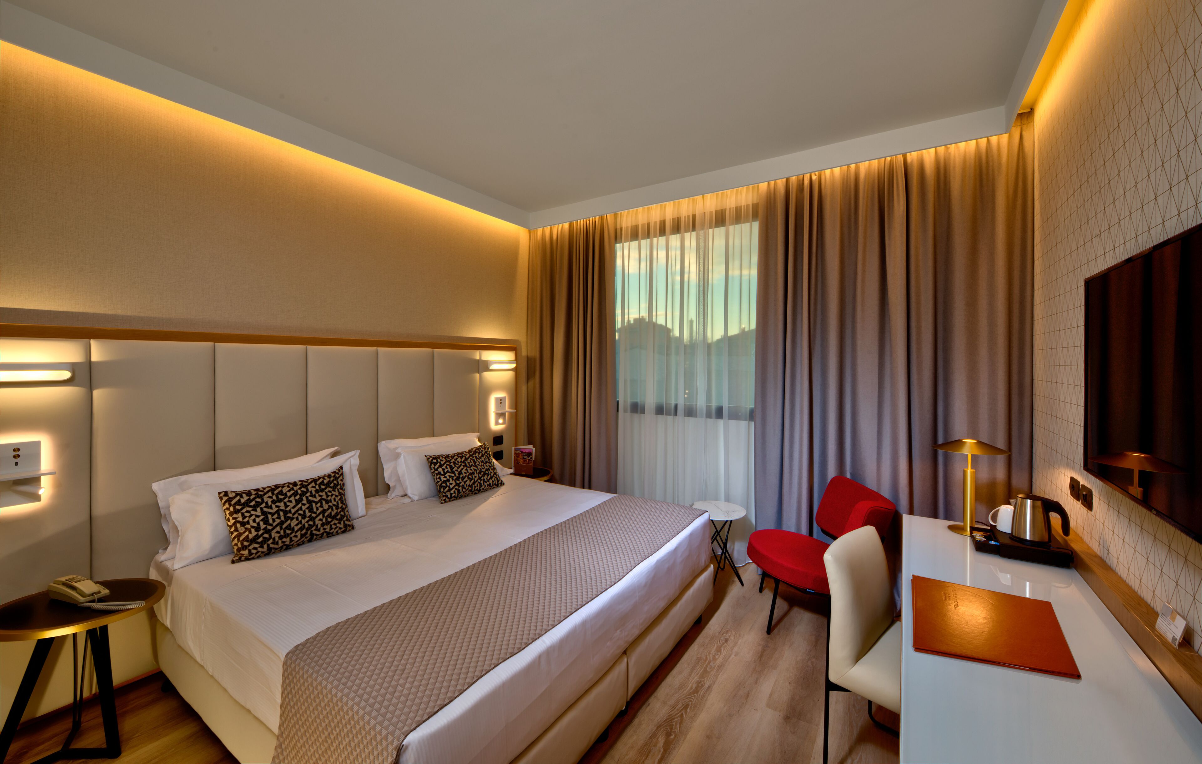 A hotel room with a large bed, a desk with a chair, a small table, and a TV.