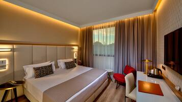 A hotel room with a large bed, a desk with a chair, a small table, and a TV.
