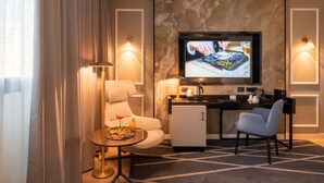 Una habitación de hotel moderna con zona de comedor, televisor y minibar.