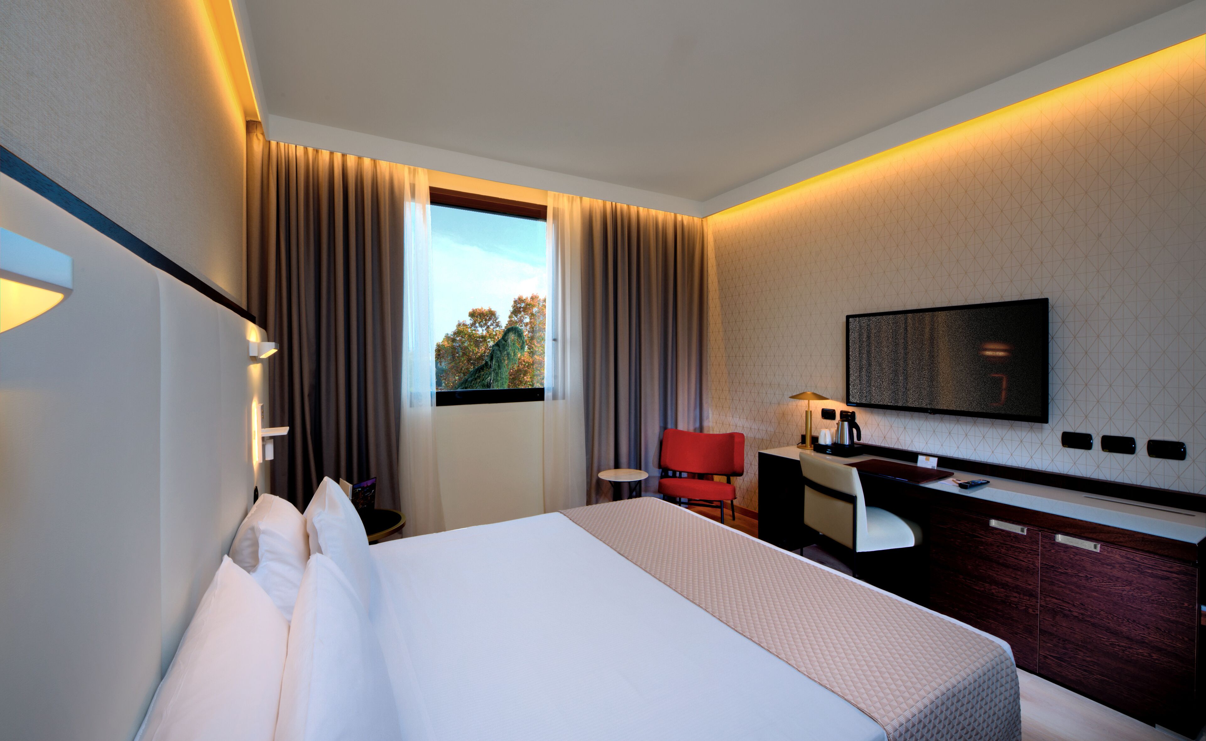Een hotelkamer met een bed, een bureau met stoel, een televisie aan de muur en een raam met gordijnen.