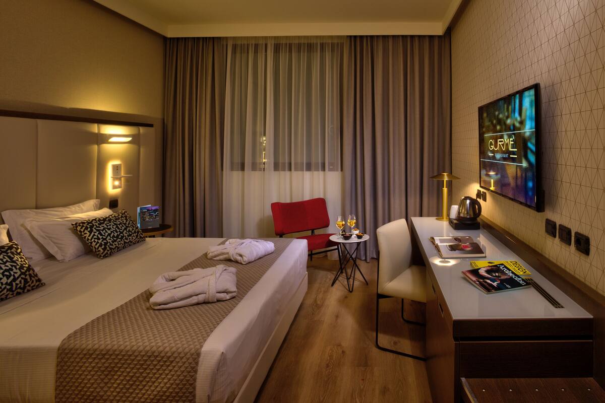 A hotel room with two beds, a desk, a chair, a TV, and a window with curtains.