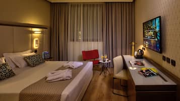 A hotel room with two beds, a desk, a chair, a TV, and a window with curtains.