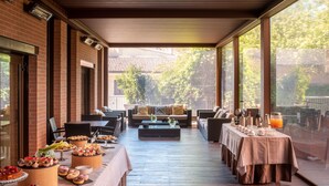 Un área de comedor al aire libre techada, con paredes de ladrillo, suelo de madera y ventanas amplias.