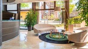 Una zona de recepción moderna con un mostrador curvo, un sofá, una mesa de centro y una planta grande en maceta.