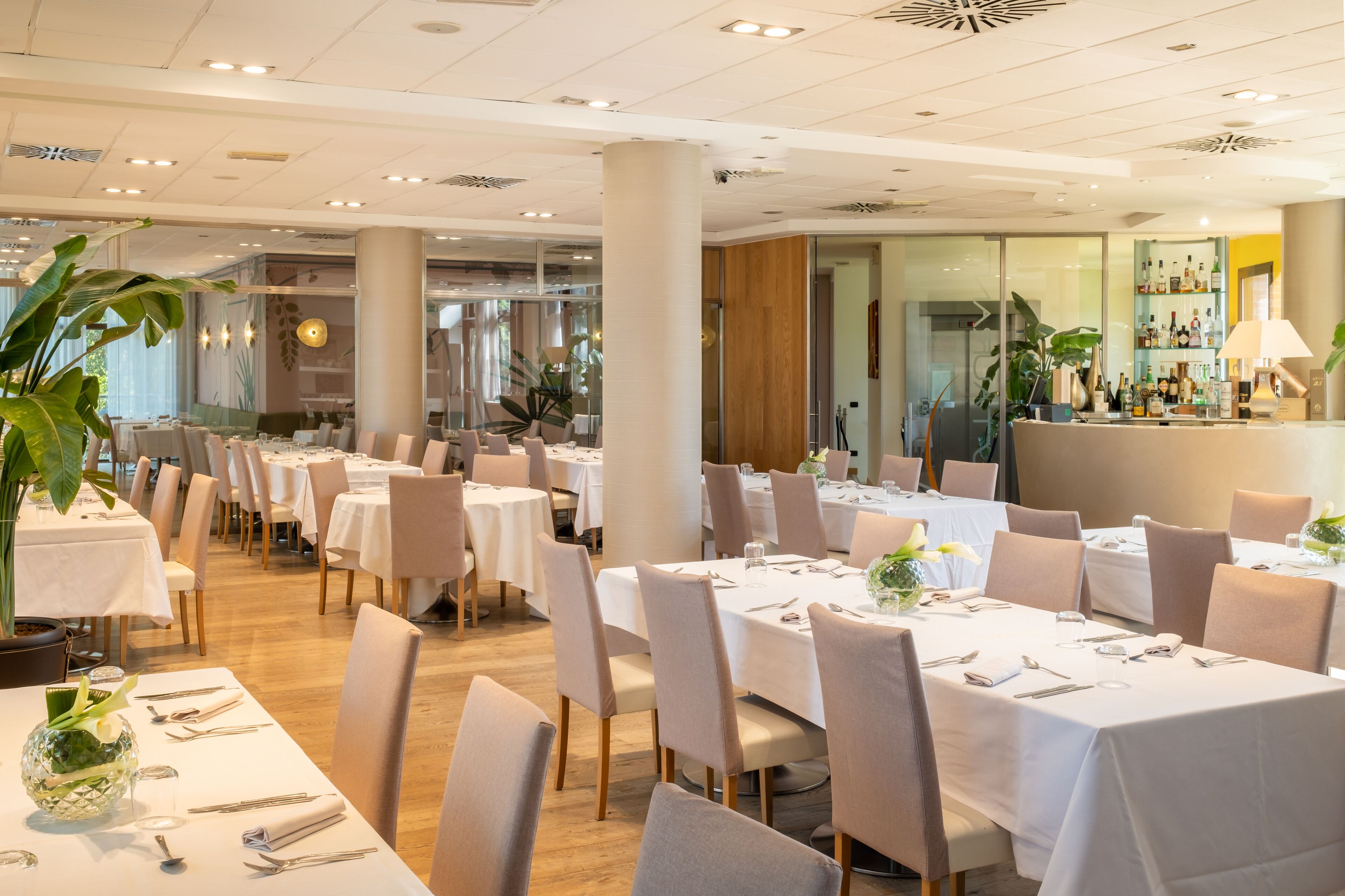 Um restaurante espaçoso com várias mesas preparadas para refeições, grandes janelas e um bar.
