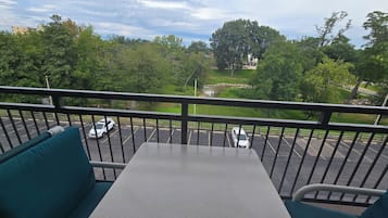 A balcony with a table and chairs, overlooking a parking area and greenery.