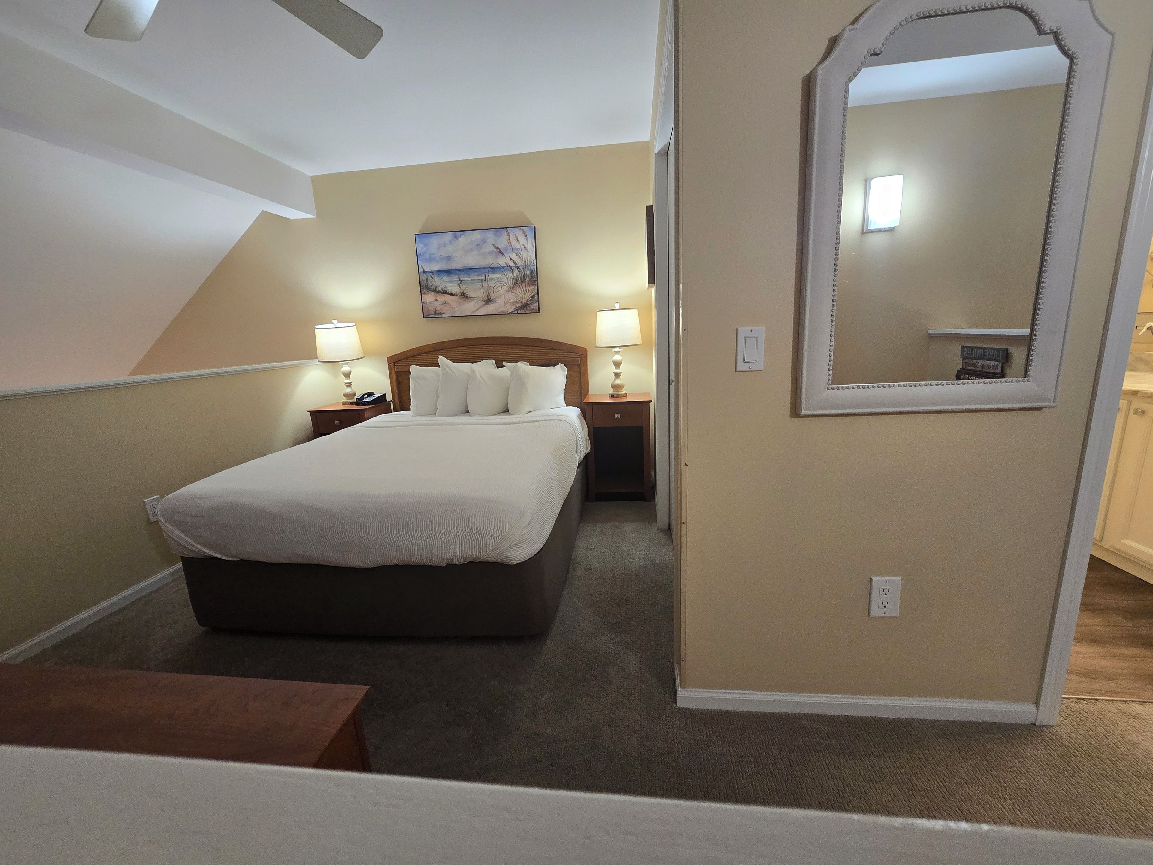 A hotel room with a bed, bedside lamps, a painting on the wall, and a mirror.