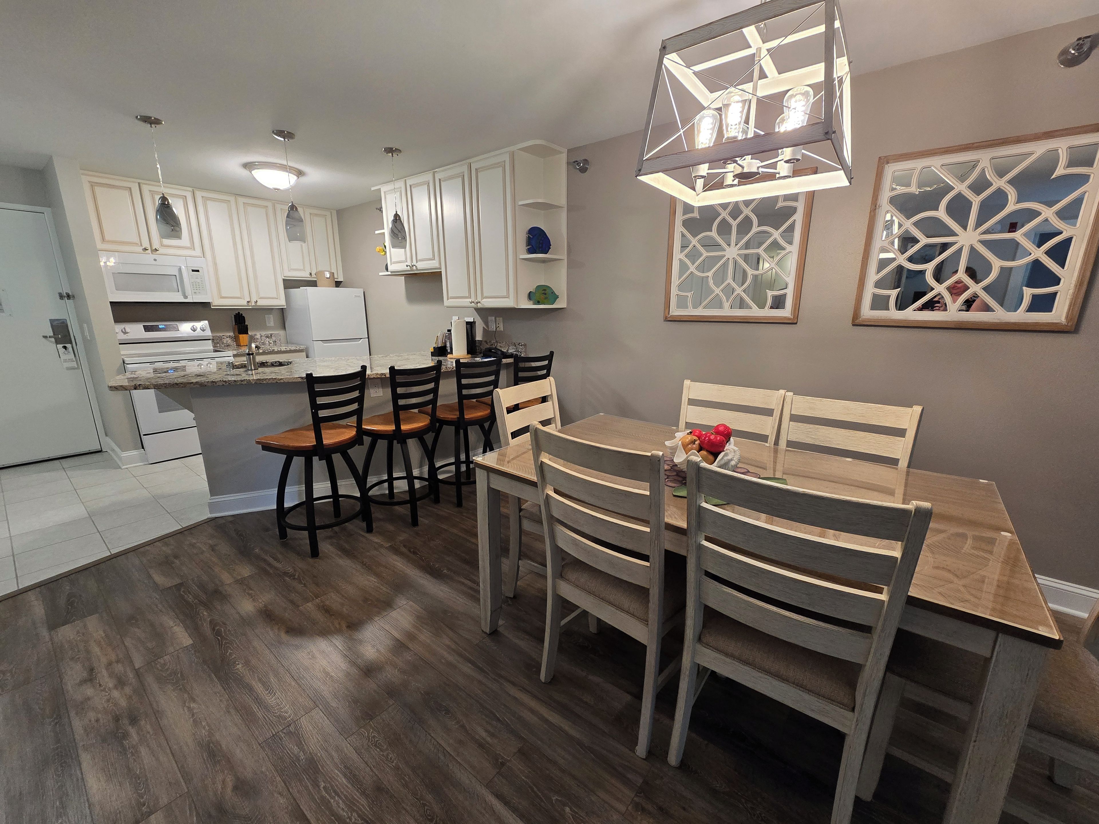 A modern kitchen with white cabinets, a dining area with wooden chairs, and a central island.