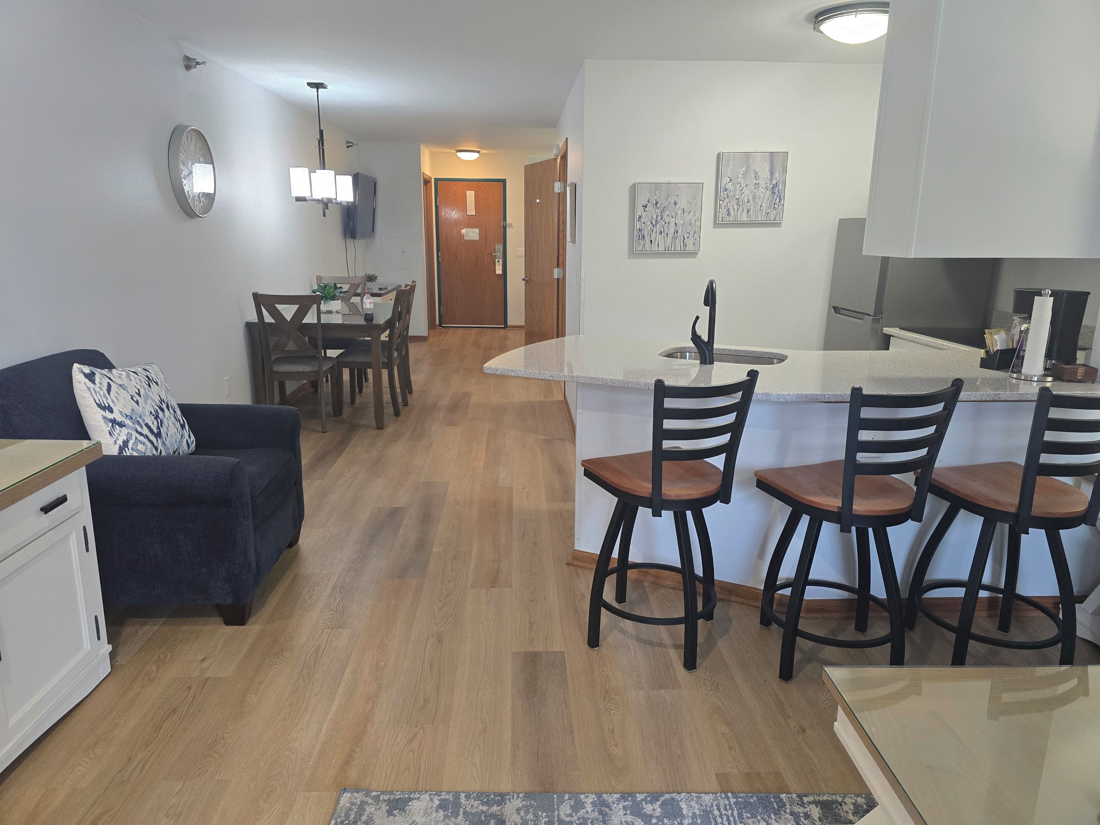 A modern kitchen with a central island, bar stools, and a dining area with a table and chairs.