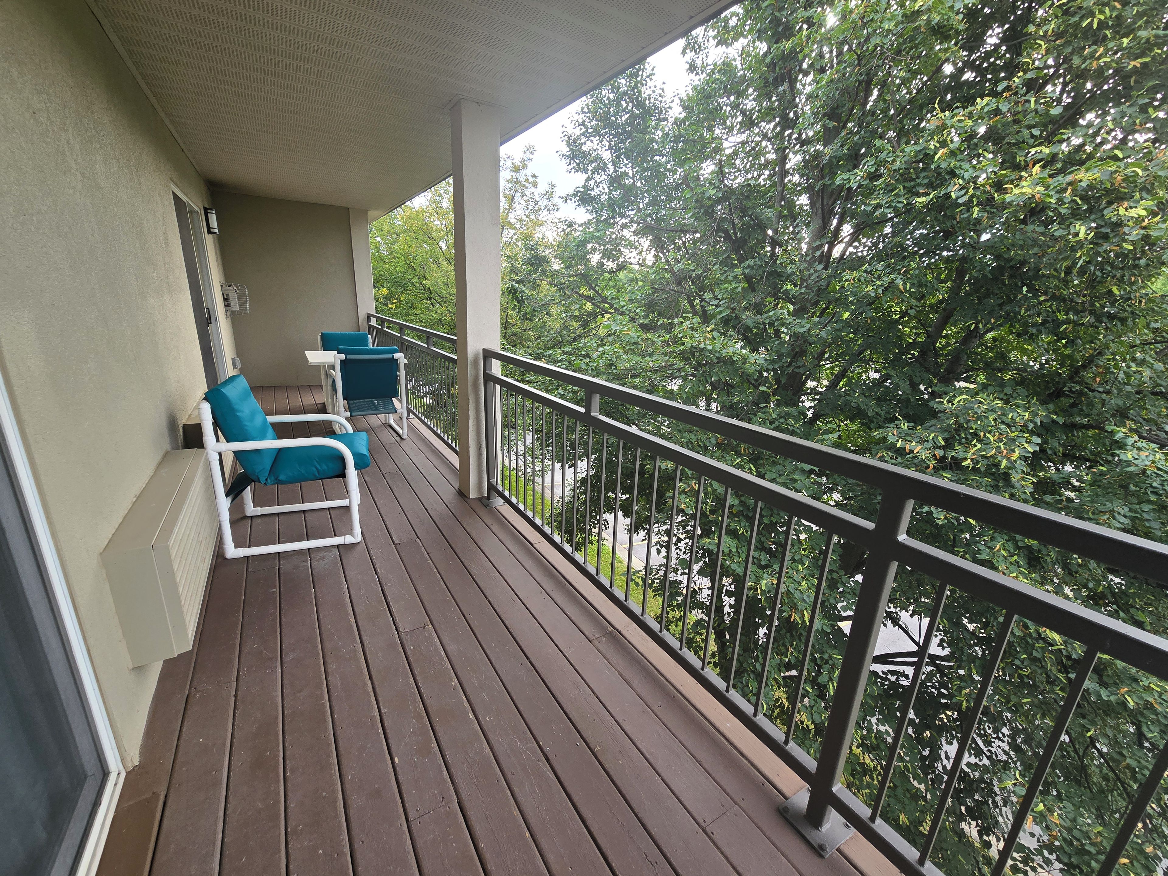 A balcony with wooden flooring and two blue chairs.