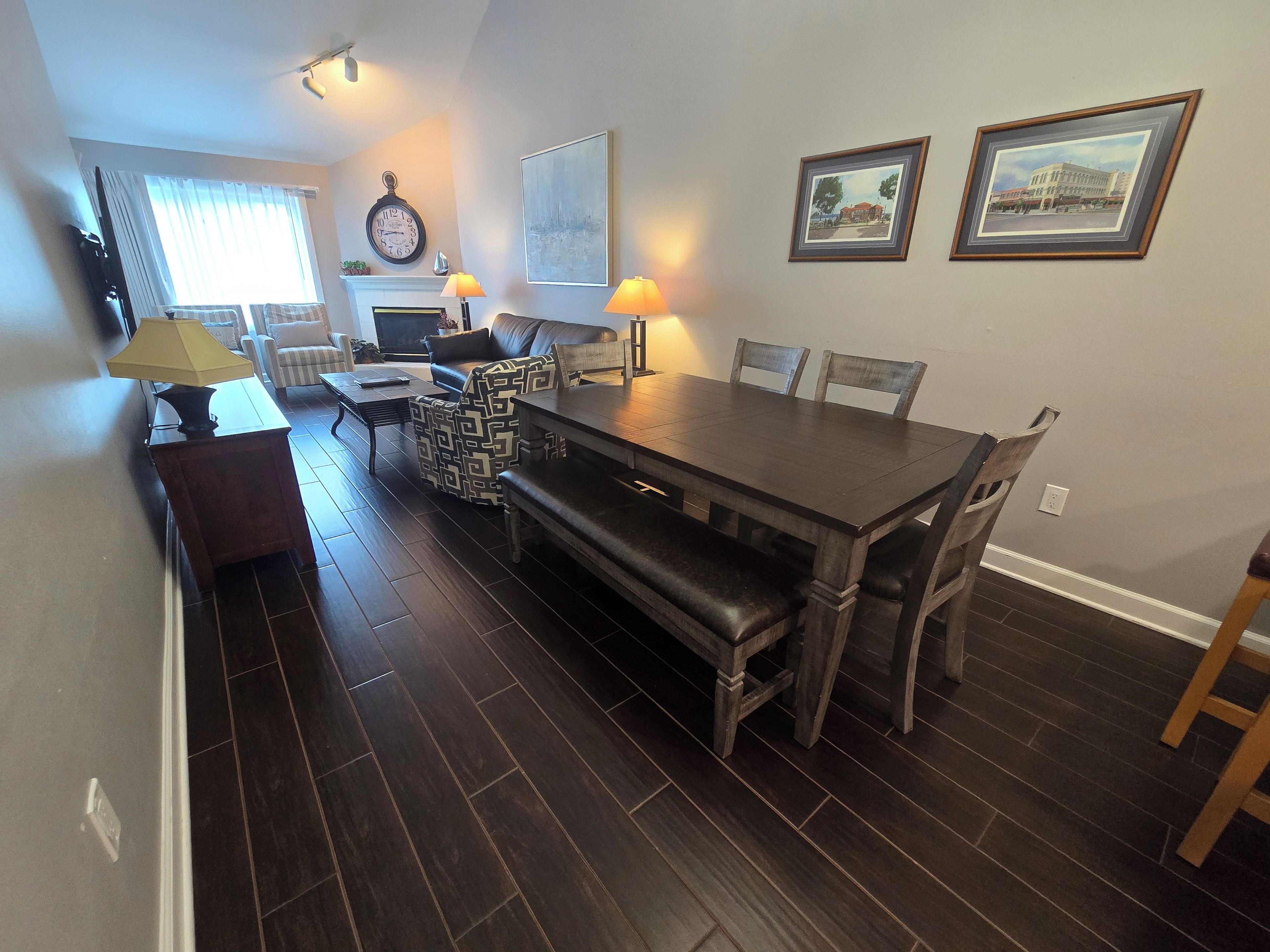 A dining area with a dark wood table, chairs, and benches, a fireplace, and wall-mounted artwork.