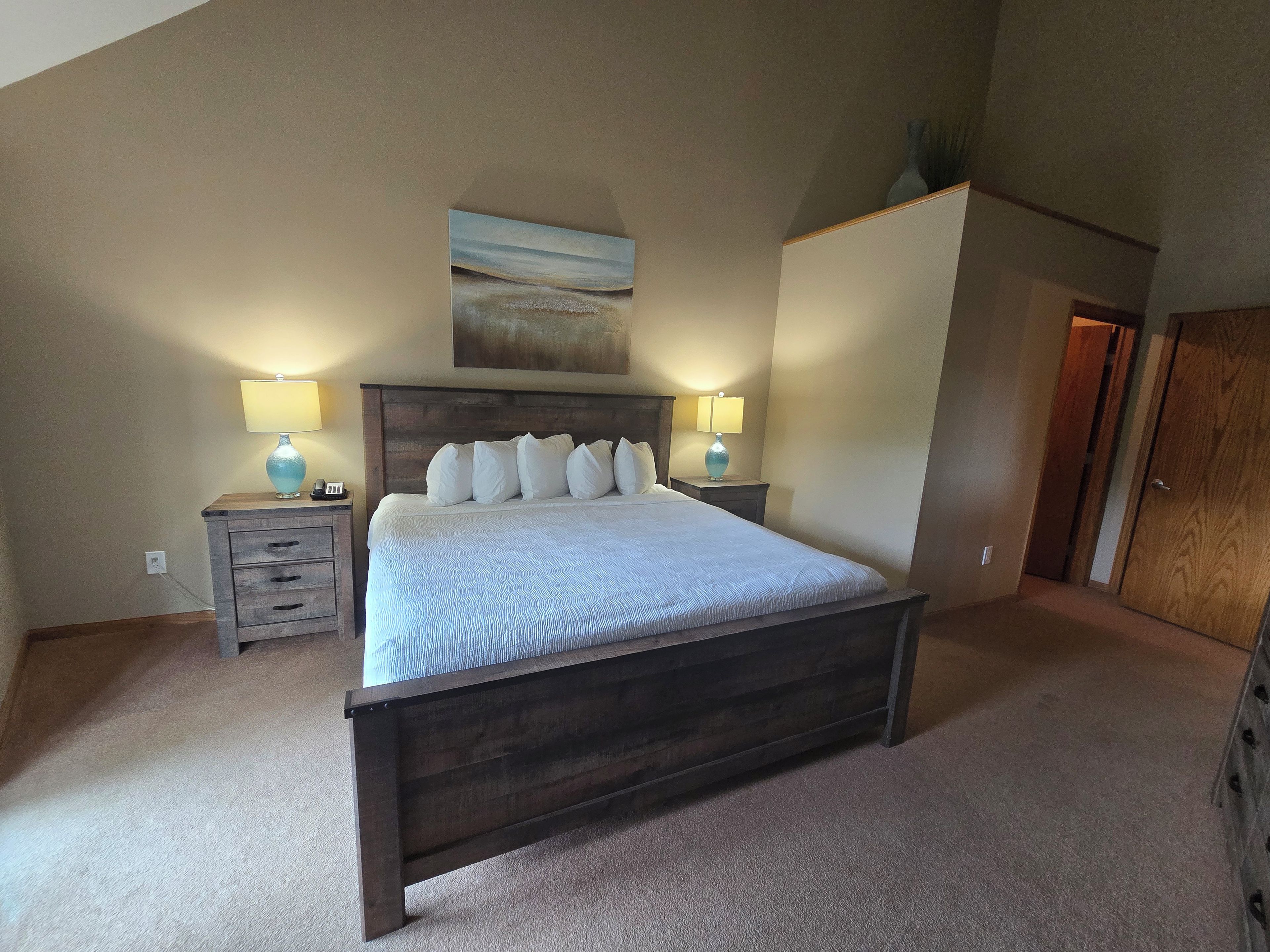Un dormitorio con una cama grande, dos mesitas de noche con lámparas, un cabecero de madera y un cuadro en la pared.