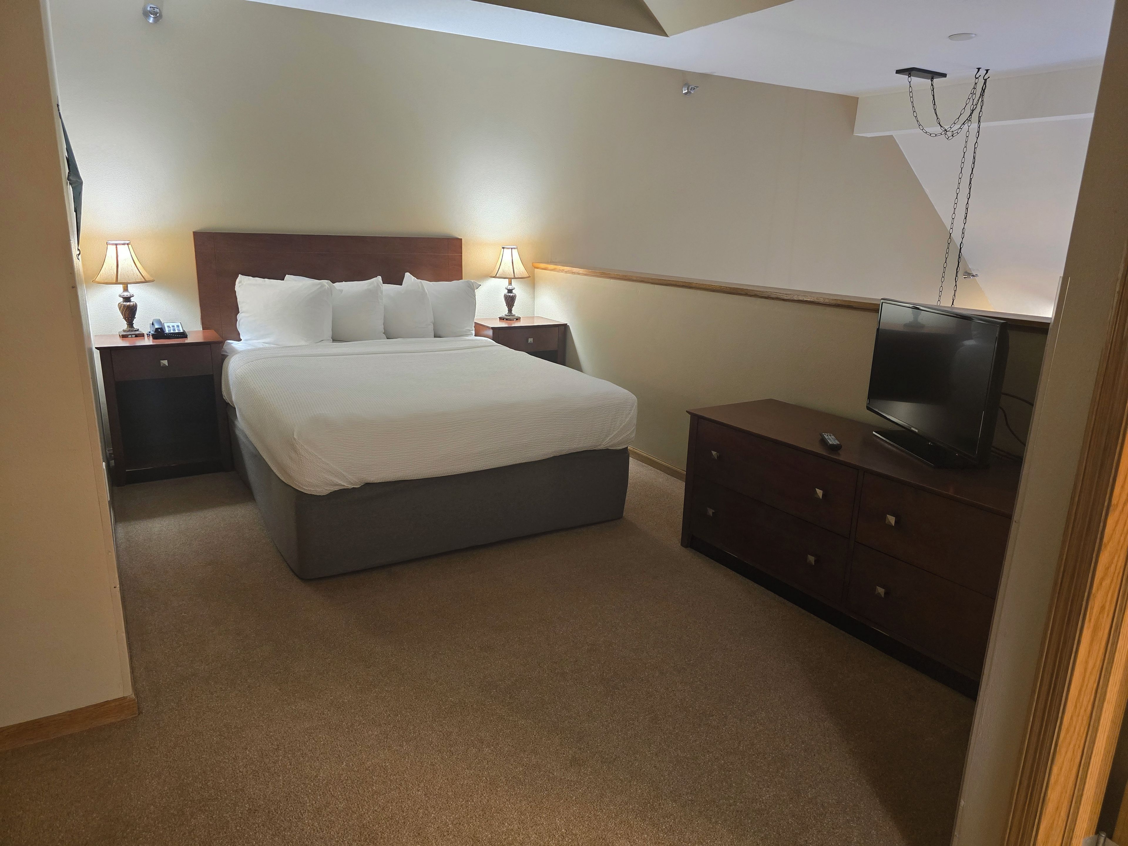 A hotel room with a bed, bedside lamps, a TV, and a dresser.