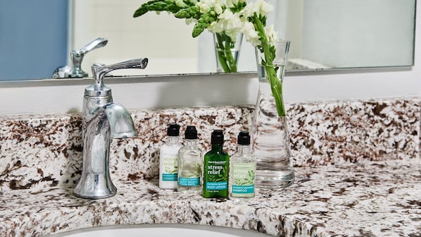 A bathroom with a granite countertop, a silver faucet, and various toiletries including body lotion and shampoo.