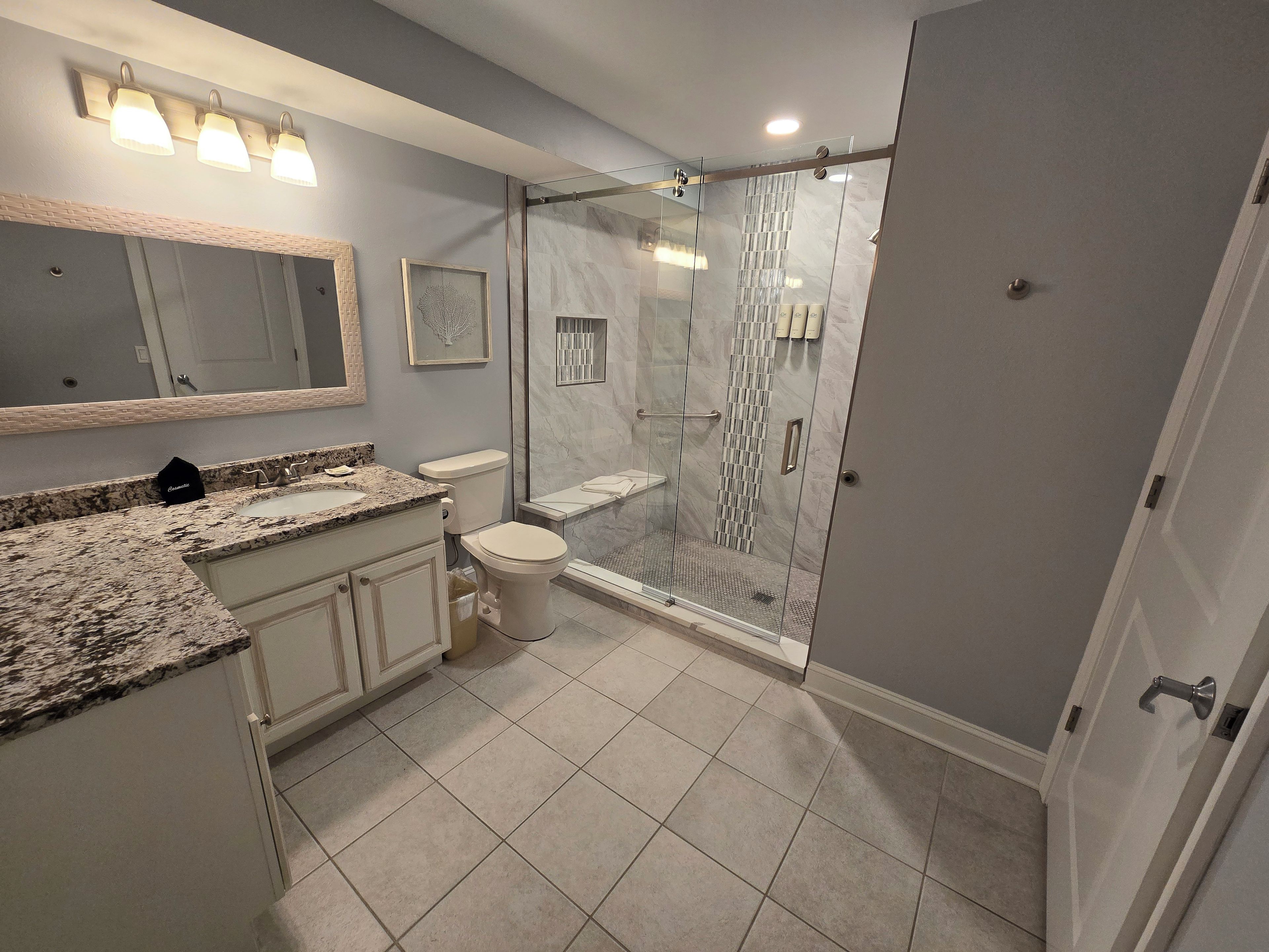 Ein modernes Badezimmer mit einer gläsernen Duschkabine, einem Waschtisch mit einer Granitplatte und einer Toilette.