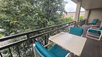 A balcony with a table and chairs, surrounded by a metal railing, overlooking a tree-lined area.