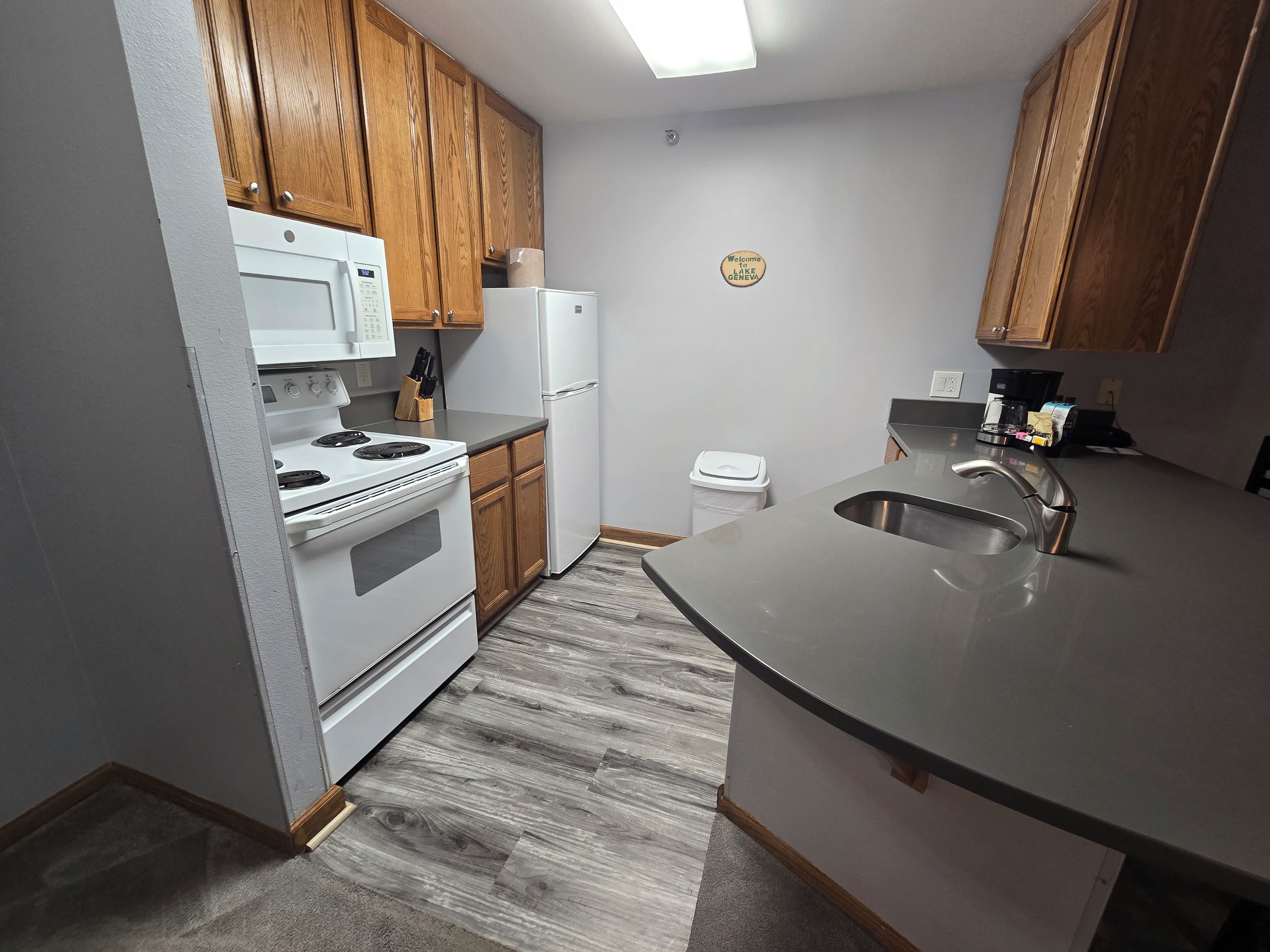 A kitchen with wooden cabinets, a white stove, a refrigerator, and a stainless steel sink.
