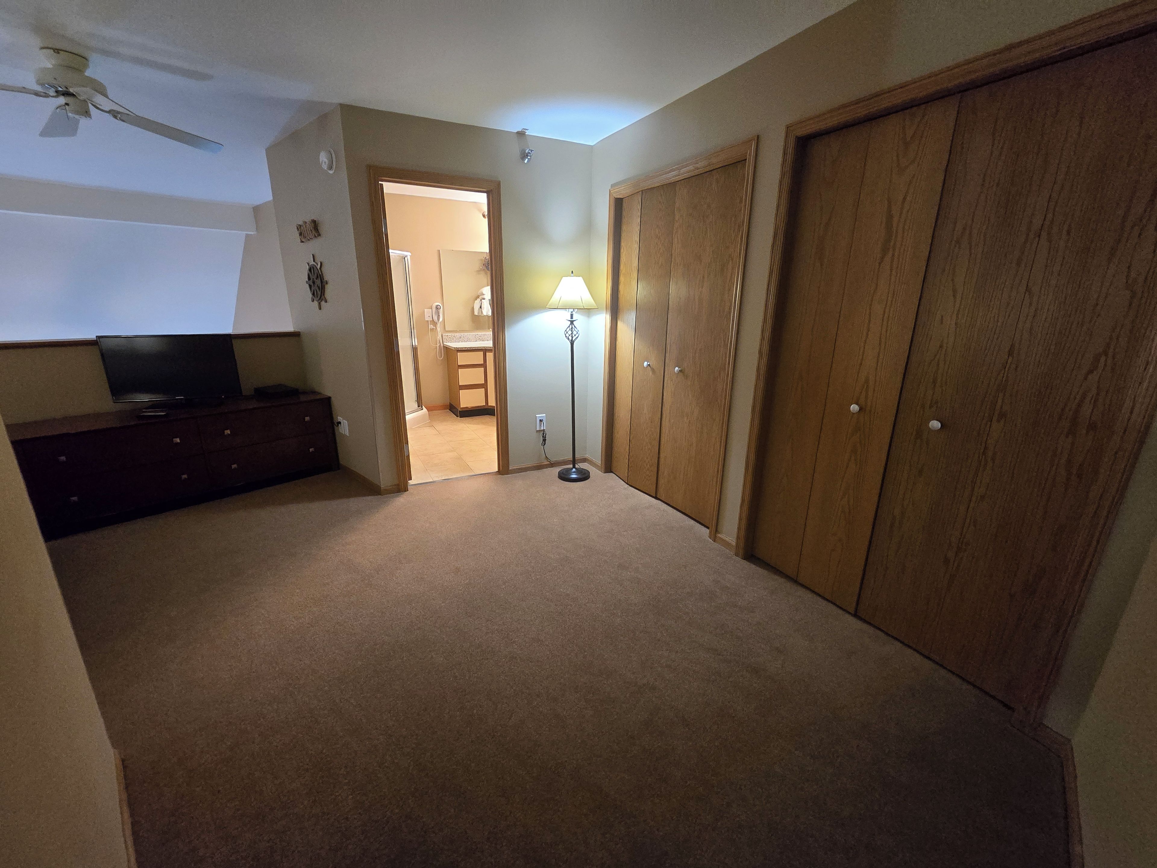 Une pièce avec un ventilateur de plafond, un téléviseur posé sur une commode, une lampe et une armoire.