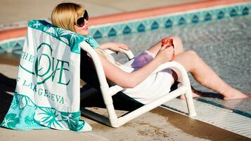 A person sitting on a poolside chair with a towel draped over their shoulders.