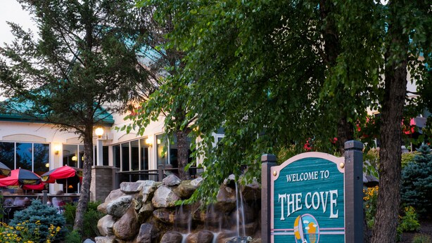 Une enseigne accueillante pour « The Cove of Lake Geneva », avec une cascade en pierre et une végétation luxuriante.