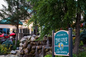 Une enseigne accueillante pour « The Cove of Lake Geneva », avec une cascade en pierre et une végétation luxuriante.