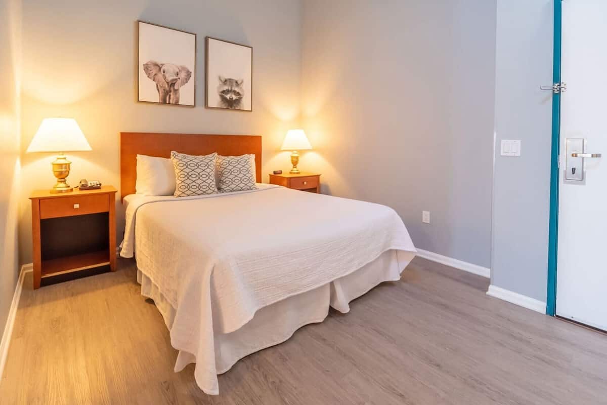 Une chambre d’hôtel avec un lit, deux lampes de chevet, une table de nuit en bois et deux tableaux encadrés accrochés au mur.