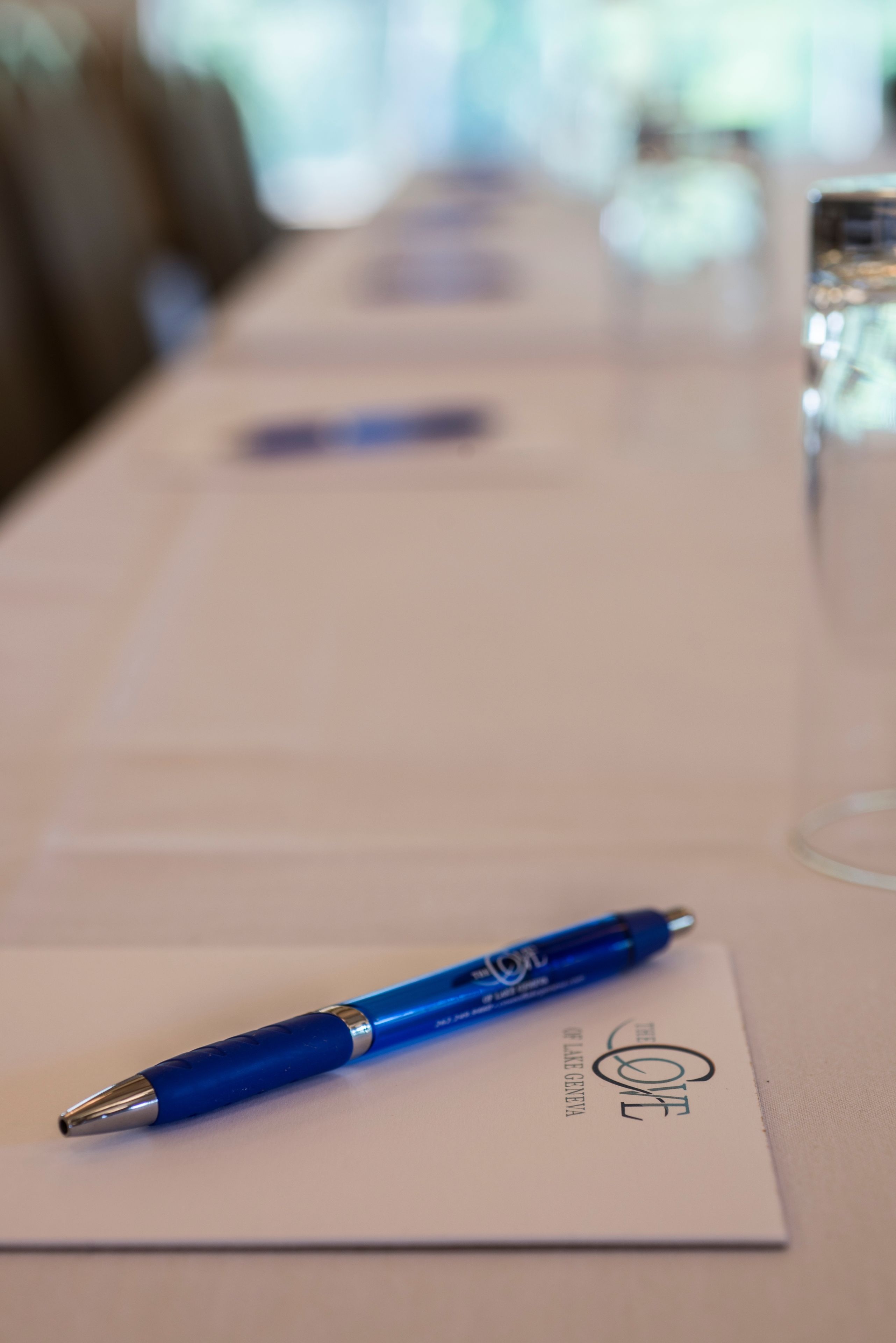 Ein Tisch mit einem blauen Stift auf einer Karte mit Text und einem Glas Wasser im Hintergrund.
