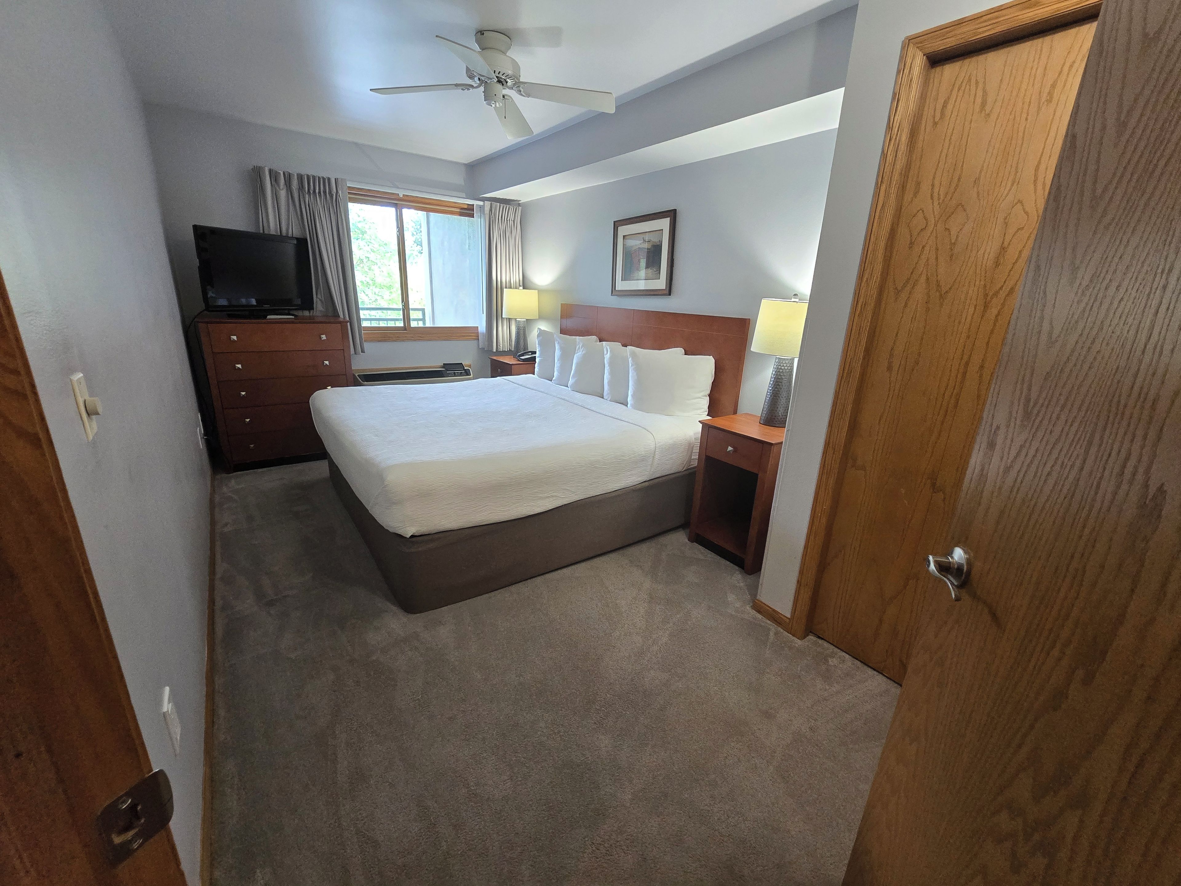 A hotel room with a bed, a television, a desk with a lamp, and a ceiling fan.