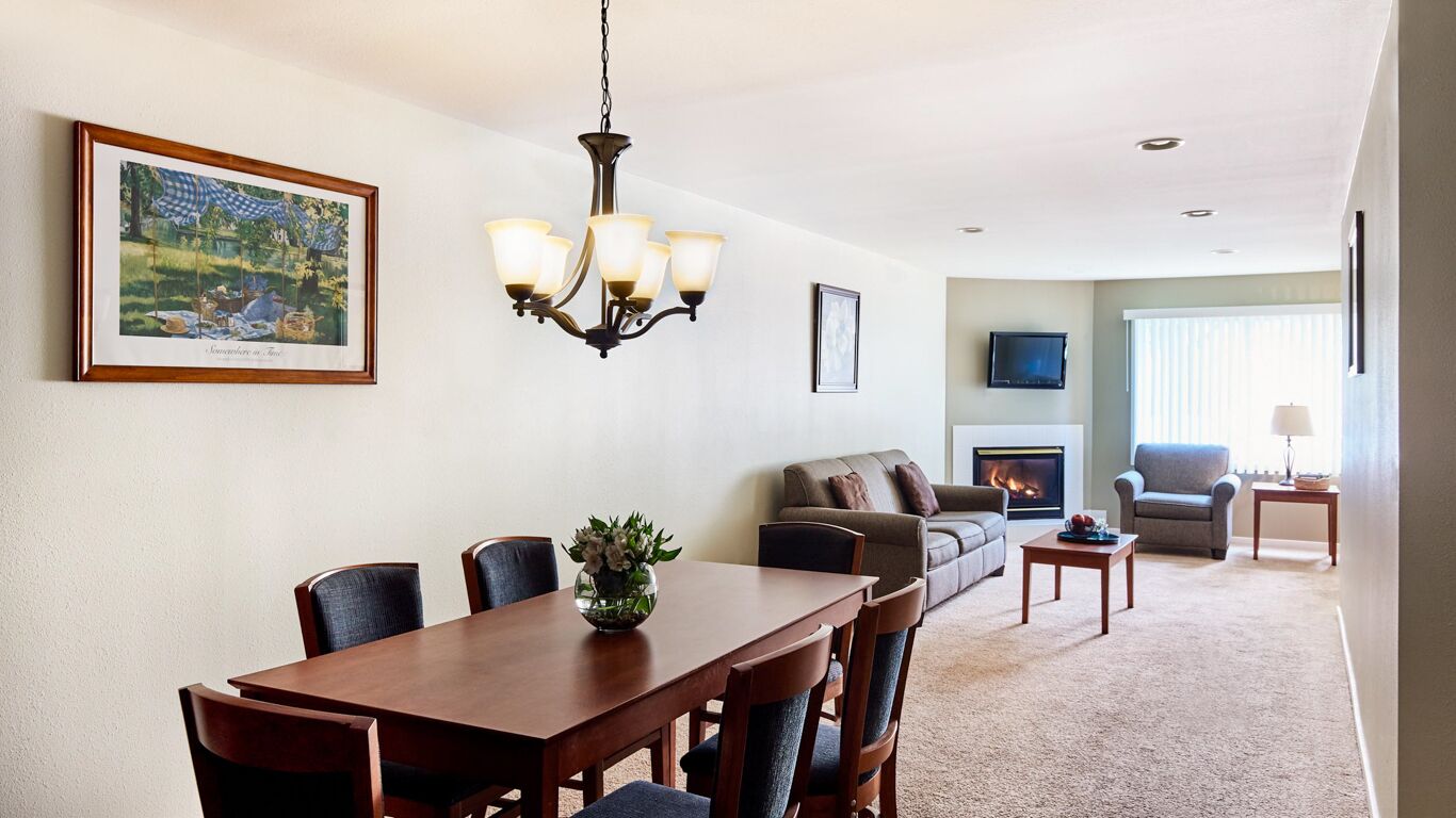 A dining area with a wooden table and chairs, a chandelier, and a fireplace in the background.