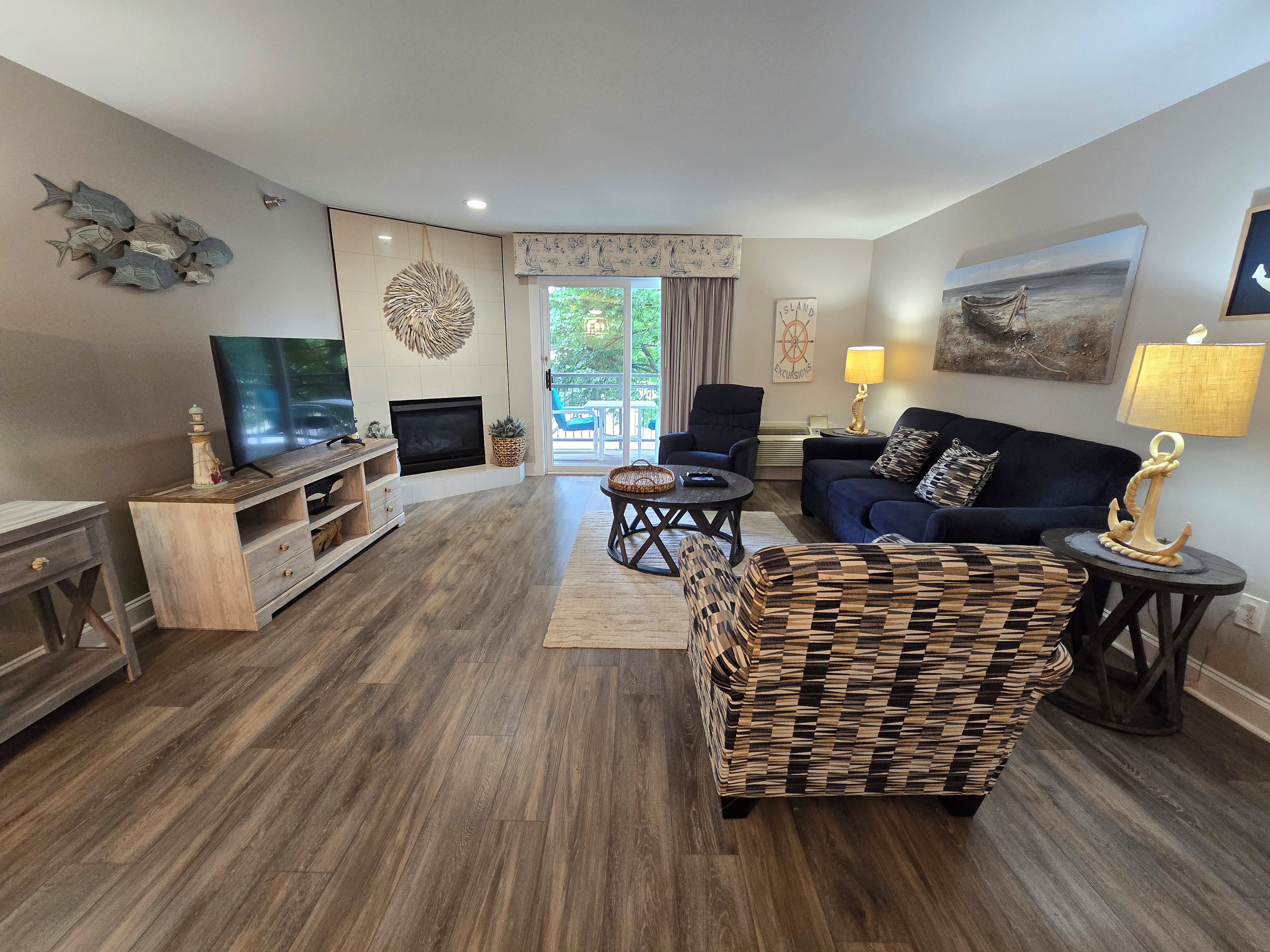 A living room with a flat-screen TV, a fireplace, a sofa, a patterned armchair, and a dining area with a table and chairs.